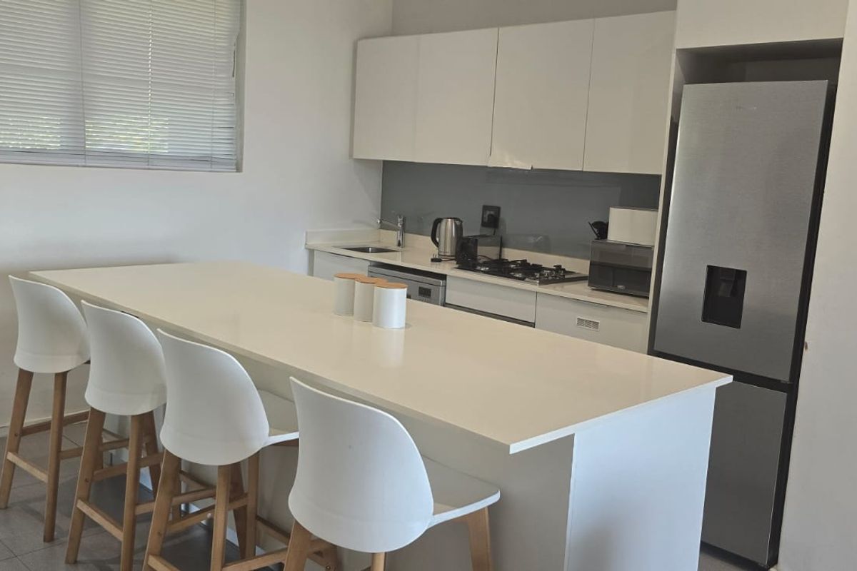 Modern kitchen featuring white cabinetry, stone countertops, a gas hob, and a breakfast bar island, complemented by tiled flooring and neutral finishes.