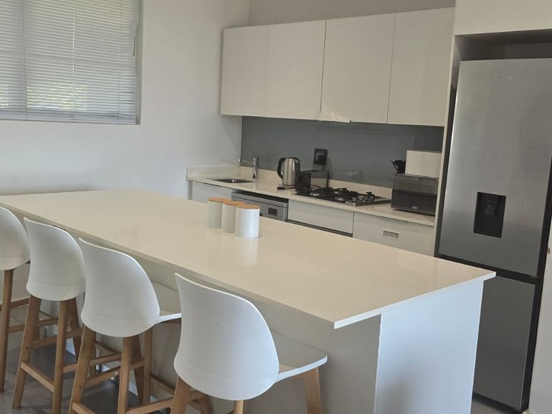 Modern kitchen featuring white cabinetry, stone countertops, a gas hob, and a breakfast bar island, complemented by tiled flooring and neutral finishes.