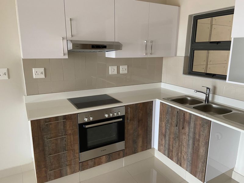 Modern kitchen featuring white upper cabinets, wood-look lower cabinetry, quartz countertops, integrated electric hob, oven, and a double bowl sink.