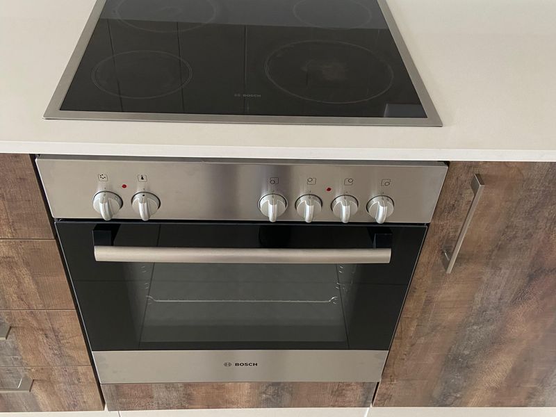 A modern kitchen featuring a built-in Bosch oven and electric cooktop, complemented by stone benchtops, tiled splashback, and wood-look cabinetry.