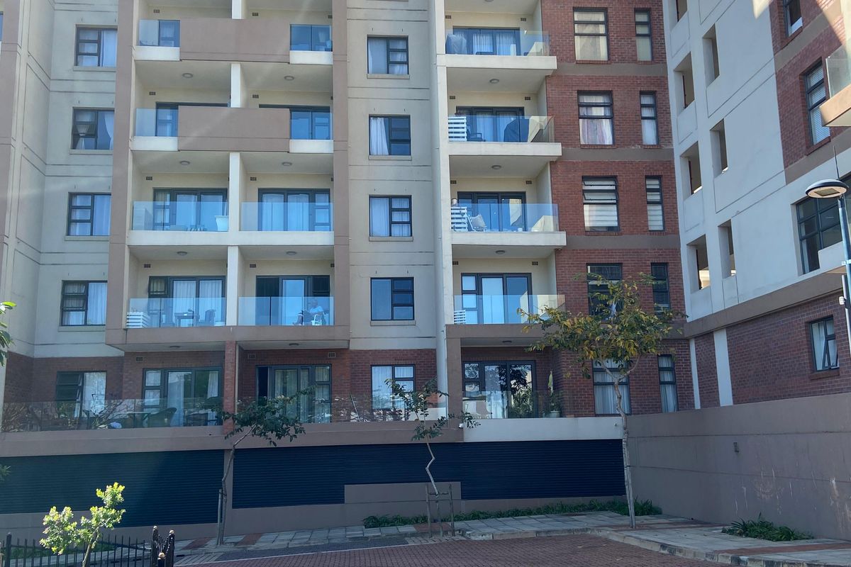 A view of the rear elevation of a modern multi-story apartment complex featuring brick and rendered facades with glass-fronted balconies and paved parking area.