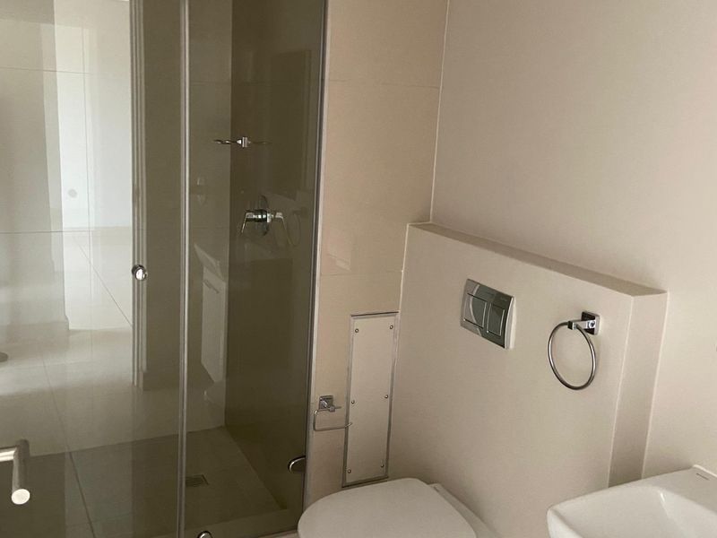 A modern bathroom featuring a wall-mounted toilet, a glass-enclosed shower, and a vanity basin with neutral tiling.