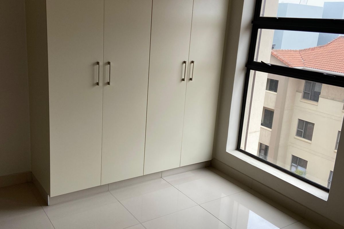 A bright, empty bedroom featuring neutral tiled flooring and floor-to-ceiling built-in cupboards, offering a clean and versatile space.