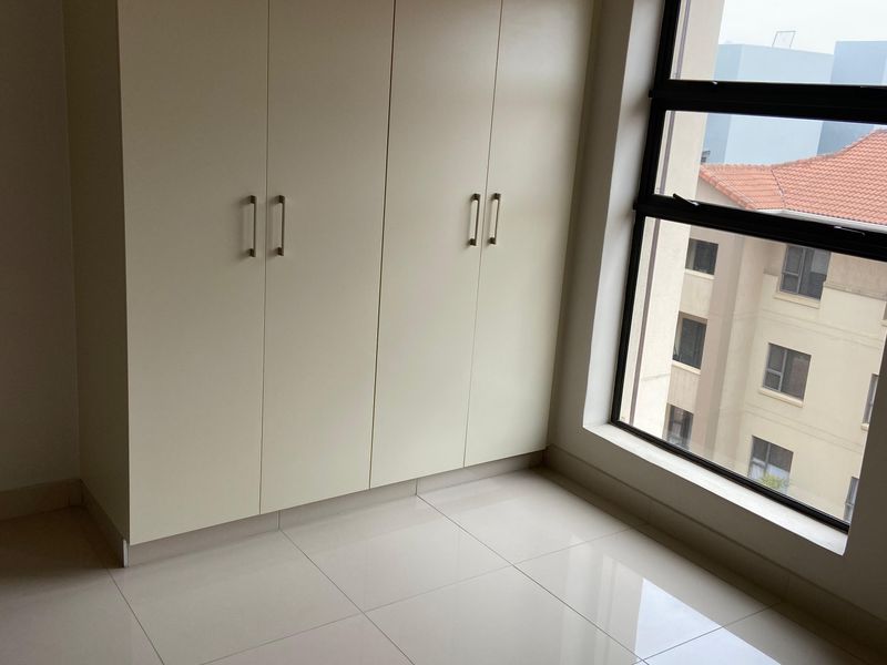 A bright, empty bedroom featuring neutral tiled flooring and floor-to-ceiling built-in cupboards, offering a clean and versatile space.
