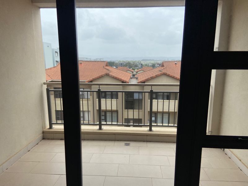 A covered balcony featuring tiled flooring and a metal balustrade, offering an elevated view of the surrounding apartment complex.