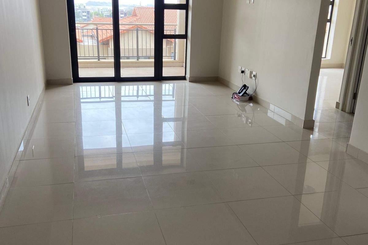 A bright, spacious, and empty living area featuring polished tiled flooring, recessed lighting, and a large sliding glass door leading to a balcony.