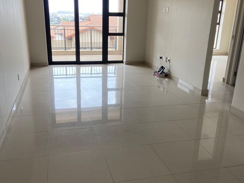 A bright, spacious, and empty living area featuring polished tiled flooring, recessed lighting, and a large sliding glass door leading to a balcony.