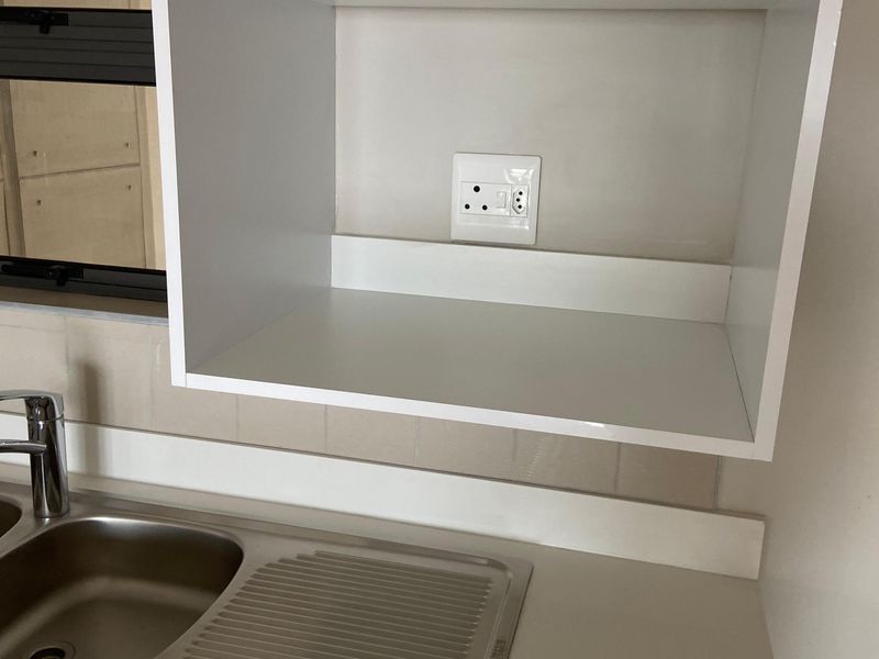 A clean kitchen area featuring a stainless steel sink, mixer tap, tiled splashback, and built-in cabinetry with an integrated electrical outlet.