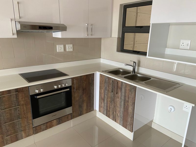 Modern kitchen featuring sleek white and wood-grain cabinetry, stone countertops, integrated Bosch oven and hob, and a double sink with tiled splashback.