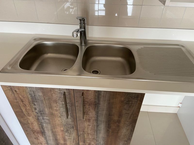 A clean kitchen area featuring a double bowl stainless steel sink with a chrome mixer tap, set into a laminate countertop with tiled splashback.