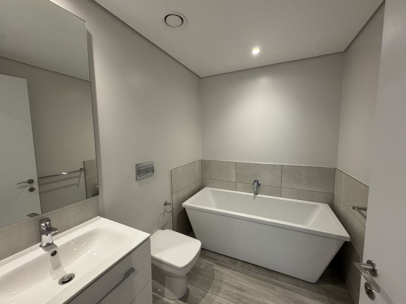 Modern bathroom featuring a sleek freestanding bathtub, wall-mounted toilet, and a contemporary vanity with integrated basin and large mirror.