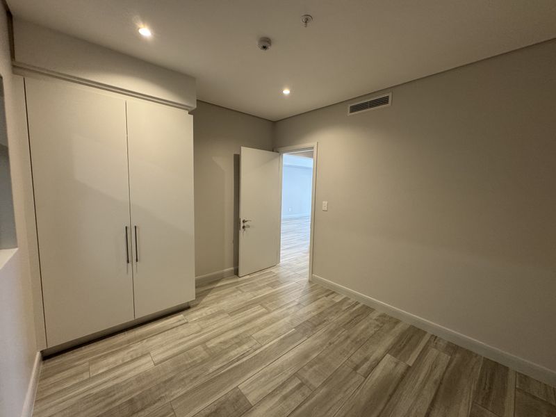 A clean, modern bedroom featuring neutral tiled flooring, built-in cabinetry, and recessed lighting, presenting a bright and well-maintained space.