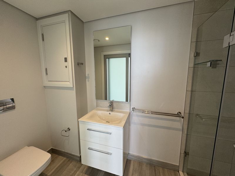 A modern, well-maintained bathroom featuring a vanity unit, wall-mounted mirror, glass shower screen, and neutral tiled flooring.