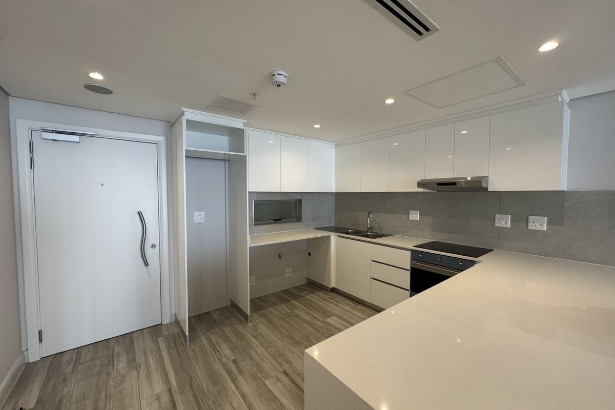 Modern kitchen featuring sleek white cabinetry, stone countertops, integrated appliances, and wood-look flooring in a clean, minimalist apartment setting.