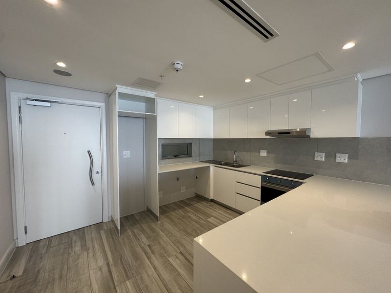 Modern kitchen featuring sleek white cabinetry, stone countertops, integrated appliances, and wood-look flooring in a clean, minimalist apartment setting.