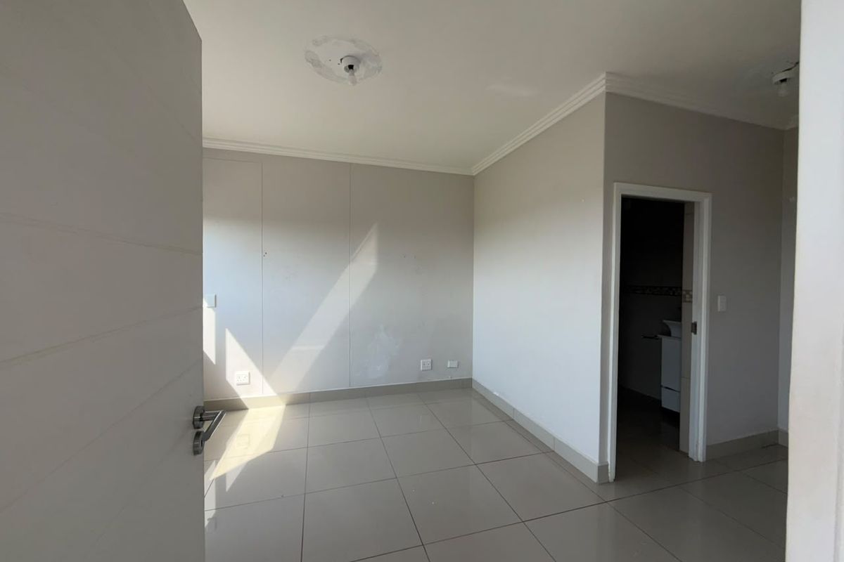 An empty bedroom featuring tiled flooring, neutral walls, and coving, with an adjacent doorway leading to an en-suite bathroom.