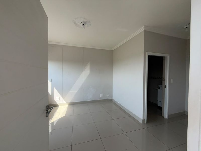 An empty bedroom featuring tiled flooring, neutral walls, and coving, with an adjacent doorway leading to an en-suite bathroom.