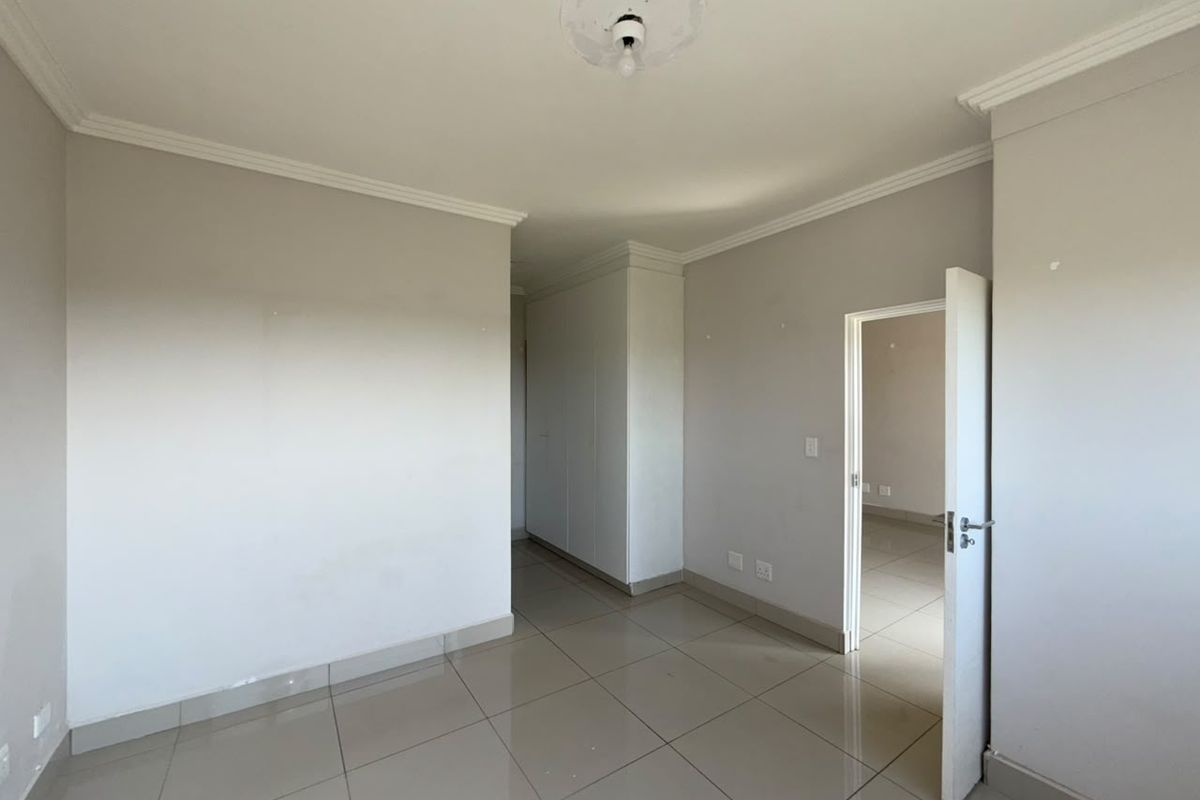 An empty bedroom featuring tiled flooring, built-in cupboards, and ceiling cornice detailing, offering a blank canvas for personalization.