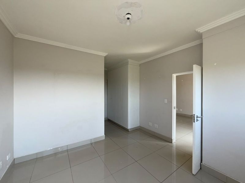 An empty bedroom featuring tiled flooring, built-in cupboards, and ceiling cornice detailing, offering a blank canvas for personalization.