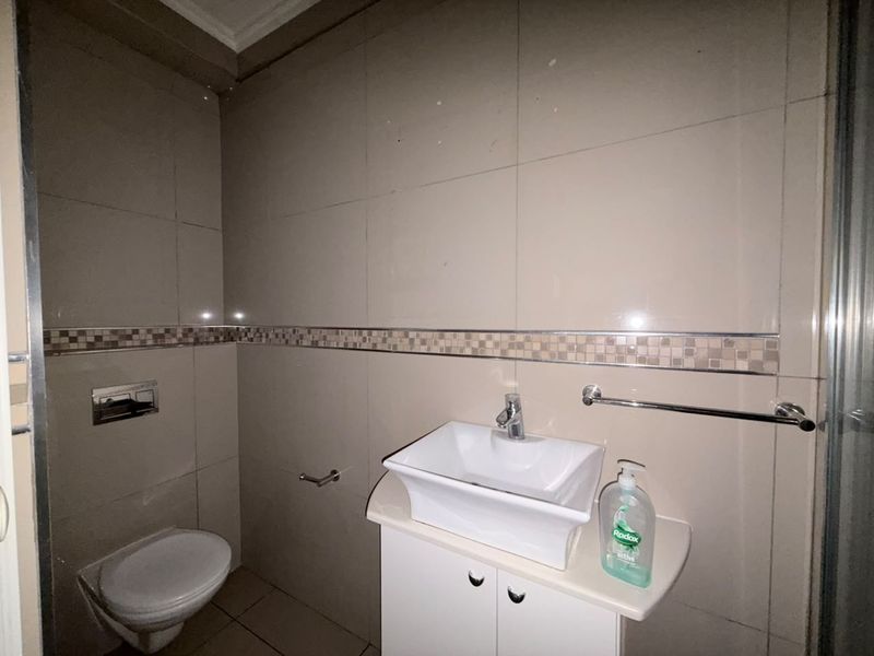 A compact bathroom featuring a wall-mounted toilet, a modern vessel sink with a vanity cabinet, and neutral wall tiling.