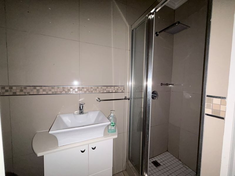 A functional bathroom featuring a vessel sink vanity, tiled walls with a mosaic border, and a glass-enclosed shower with a rainfall shower head.