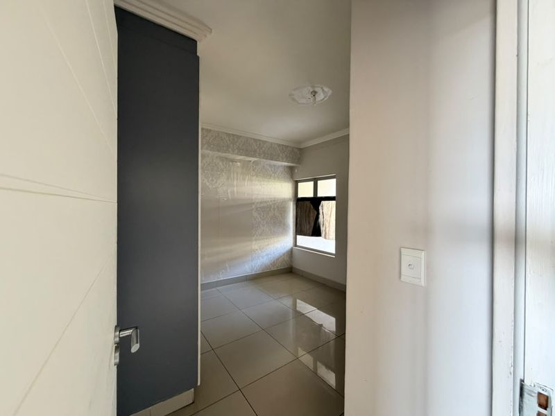 An empty bedroom featuring tiled flooring, a ceiling rose, and a window, currently requiring cosmetic updates to the wall finishes.
