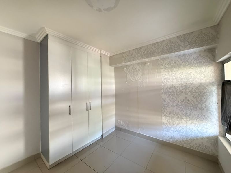 An empty bedroom featuring built-in cupboards, tiled flooring, and decorative wallpaper that shows signs of wear and peeling.