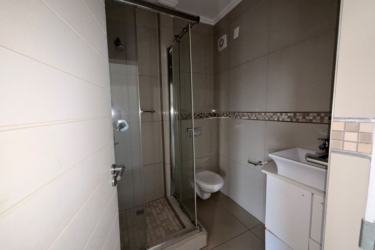 A compact bathroom featuring a glass-enclosed shower, wall-mounted toilet, and a vanity basin with tiled finishes throughout.