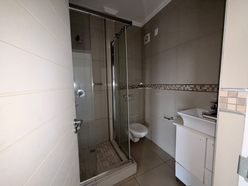 A compact bathroom featuring a glass-enclosed shower, wall-mounted toilet, and a vanity basin with tiled finishes throughout.