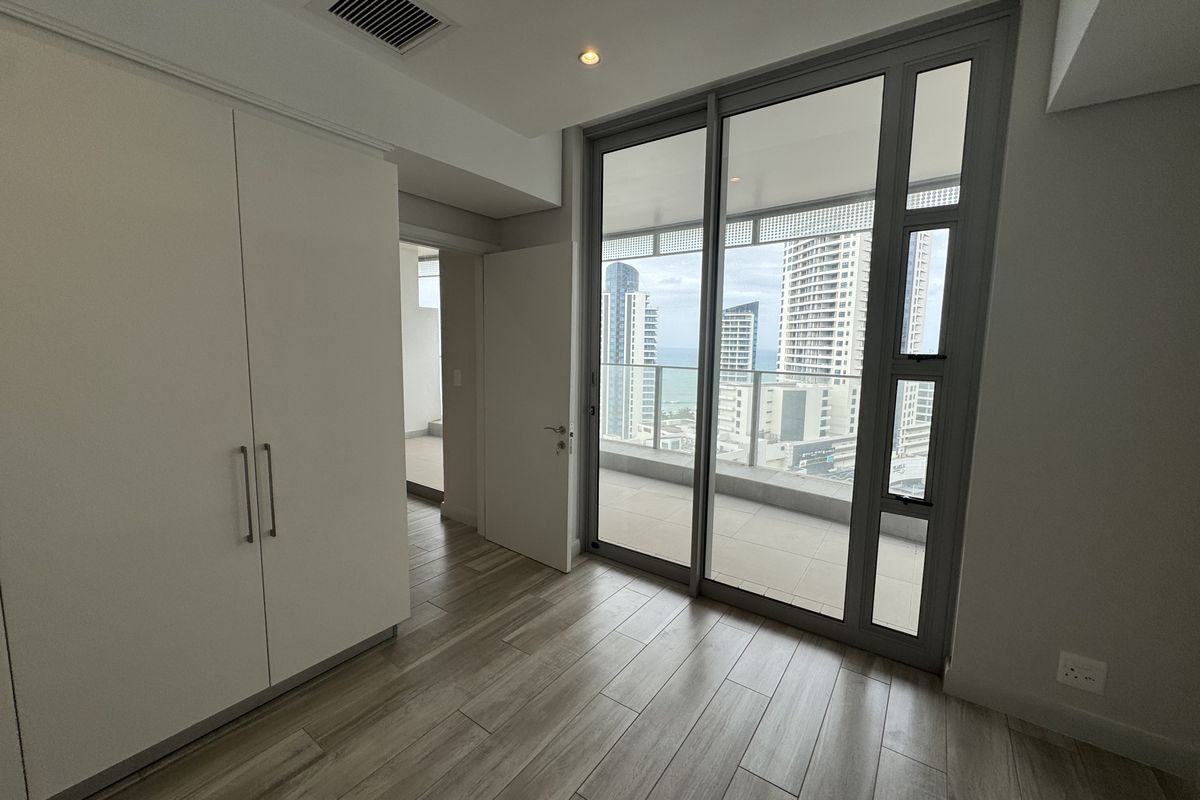 Modern bedroom featuring built-in cupboards, laminate flooring, and large sliding glass doors providing access to a balcony with city and sea views.