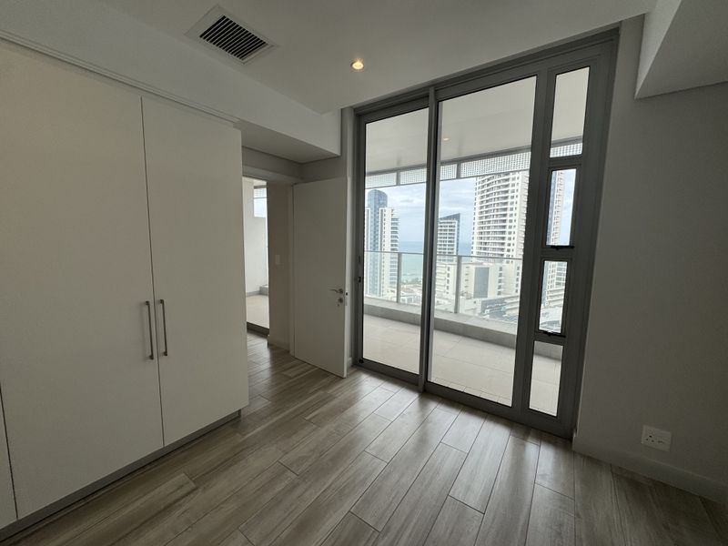 Modern bedroom featuring built-in cupboards, laminate flooring, and large sliding glass doors providing access to a balcony with city and sea views.