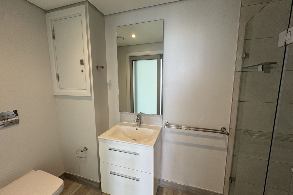 A modern, well-maintained bathroom featuring a vanity unit, wall-mounted mirror, glass shower screen, and neutral tiled flooring.