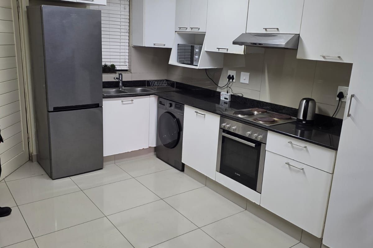 A functional kitchen featuring white cabinetry, granite countertops, integrated oven and hob, and tiled flooring, providing a clean and practical workspace.