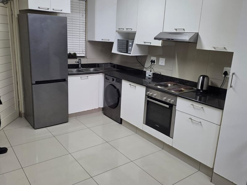 A functional kitchen featuring white cabinetry, granite countertops, integrated oven and hob, and tiled flooring, providing a clean and practical workspace.