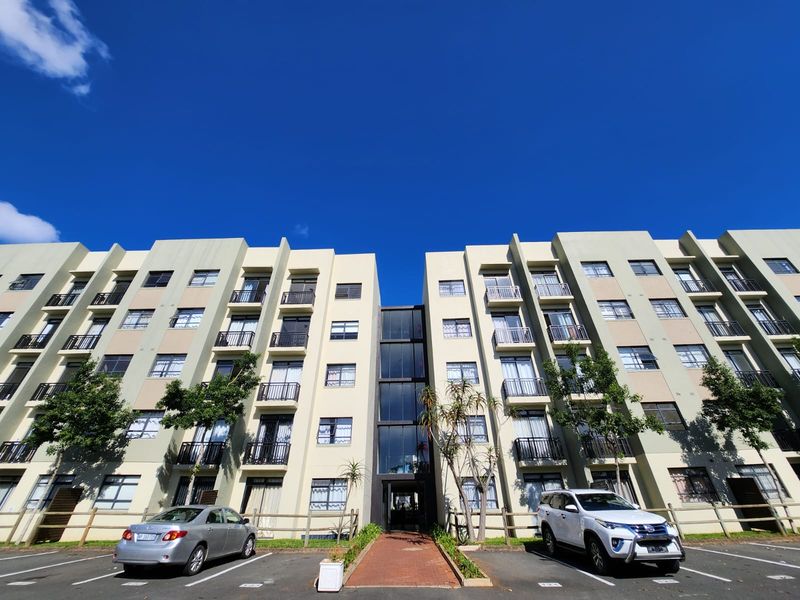 Front elevation of a multi-story apartment complex featuring private balconies, a central glass stairwell, and designated parking bays.