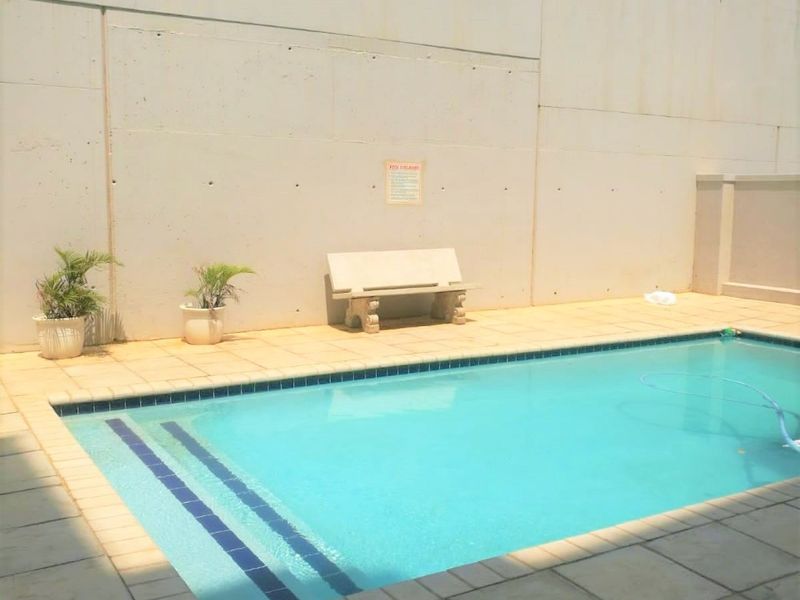 A private swimming pool area featuring a tiled surround, concrete boundary wall, and integrated electric security fencing.