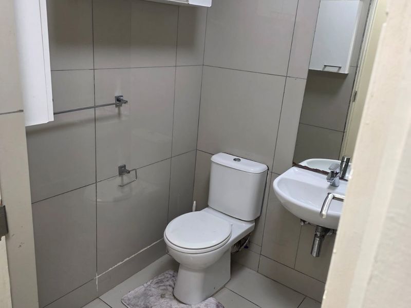 A compact bathroom featuring tiled walls and floors, a wall-mounted basin with a mixer tap, and a wall-mounted toilet.