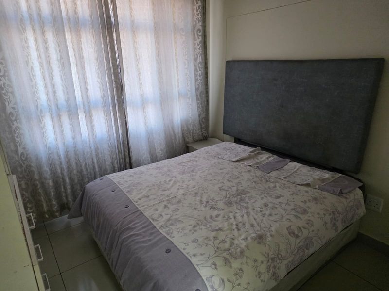 A functional bedroom featuring tiled flooring and a large window with curtains, providing a neutral space ready for personalization.