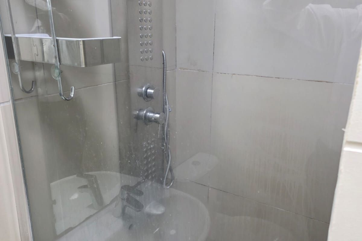 A compact bathroom featuring a glass-enclosed shower, wall-mounted basin, and tiled finishes. The space is functional but would benefit from a refresh.
