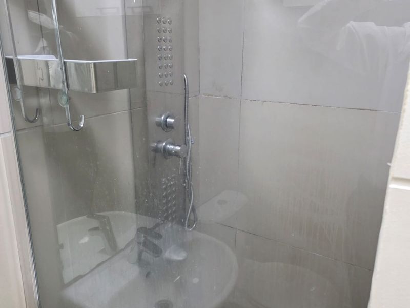 A compact bathroom featuring a glass-enclosed shower, wall-mounted basin, and tiled finishes. The space is functional but would benefit from a refresh.