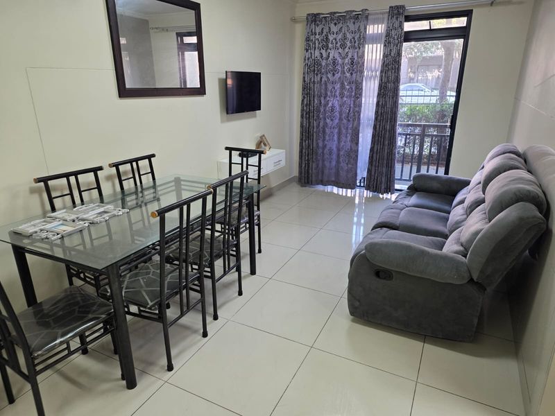 A living and dining area featuring large format floor tiles, a sliding glass door with security gate, and access to an outdoor space.