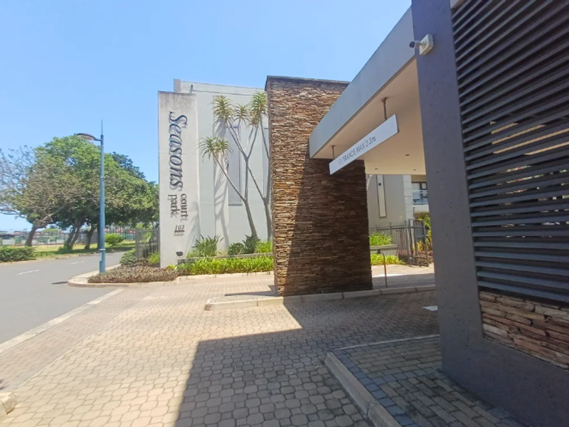 The front entrance of Seasons Court apartment complex, featuring stone cladding, paved driveway, and clear signage.