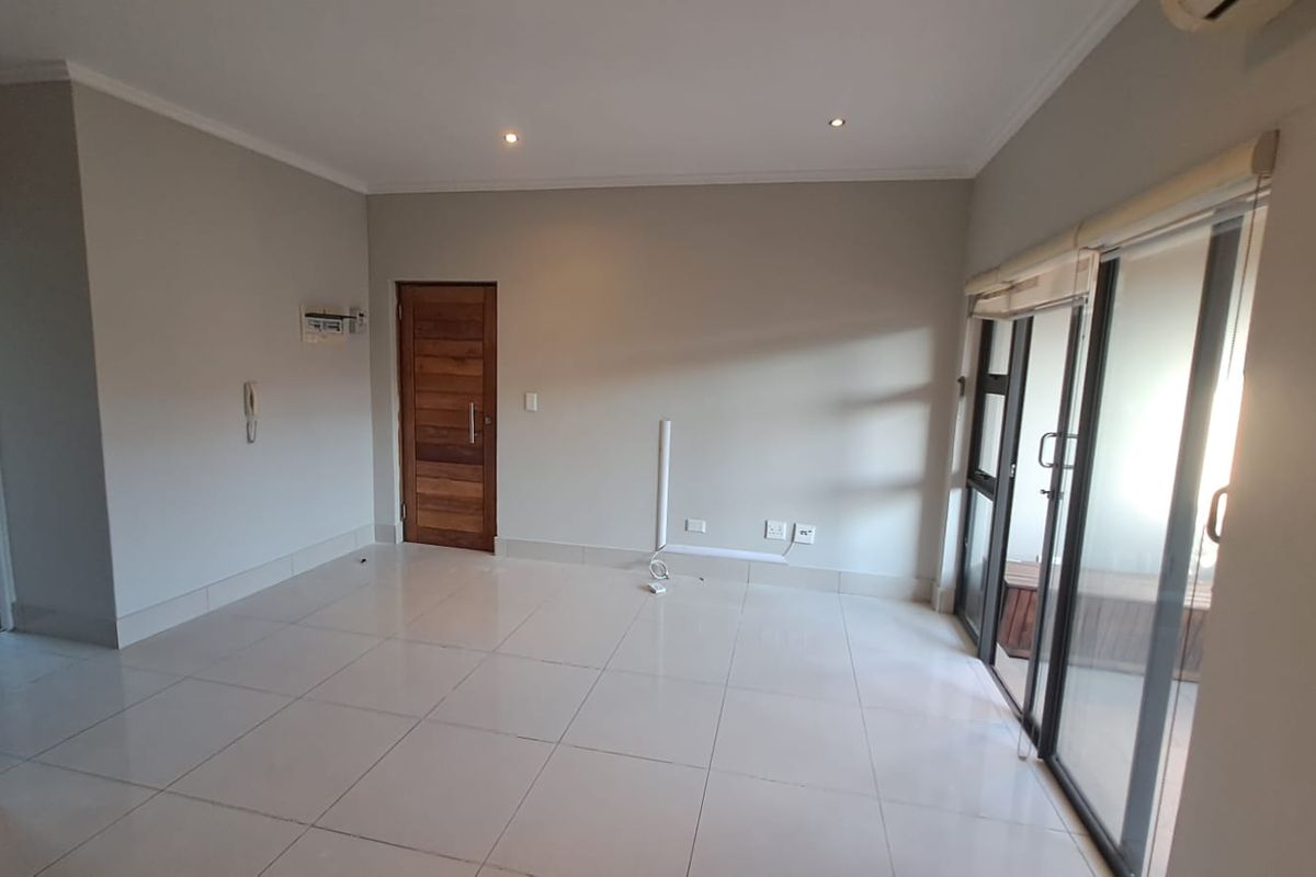 A bright, empty living room featuring neutral tiled flooring, recessed lighting, and large sliding glass doors leading to an outdoor area.