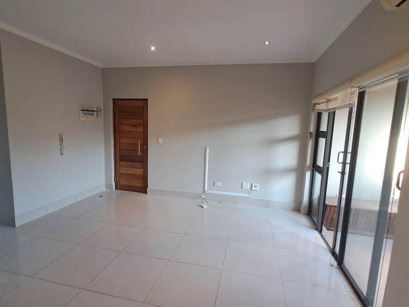 A bright, empty living room featuring neutral tiled flooring, recessed lighting, and large sliding glass doors leading to an outdoor area.