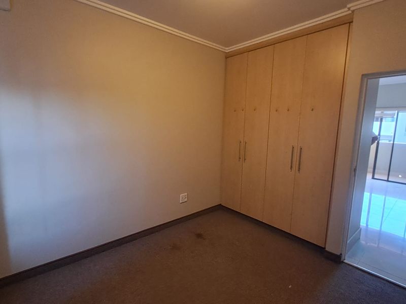 A bedroom featuring built-in wooden cupboards and carpeted flooring, with a view into an adjacent tiled living area.