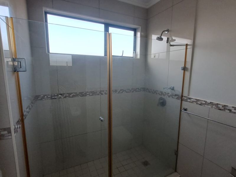 A clean, modern bathroom shower area featuring a glass enclosure, tiled walls with decorative accents, and a functional shower fixture.