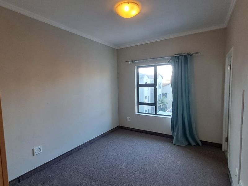 An empty bedroom featuring carpeted flooring, neutral wall tones, and an aluminium-framed window, providing a blank canvas for personalization.