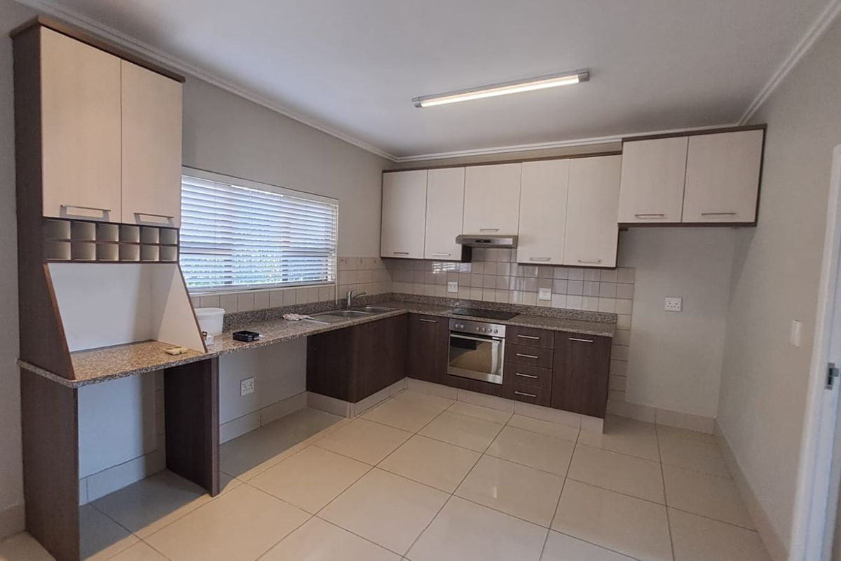 A clean, modern kitchen featuring granite countertops, built-in oven, electric hob, extractor fan, and ample storage cabinetry with neutral tiled flooring.