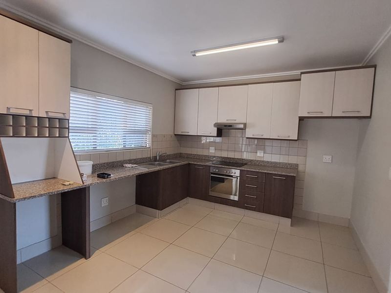 A clean, modern kitchen featuring granite countertops, built-in oven, electric hob, extractor fan, and ample storage cabinetry with neutral tiled flooring.