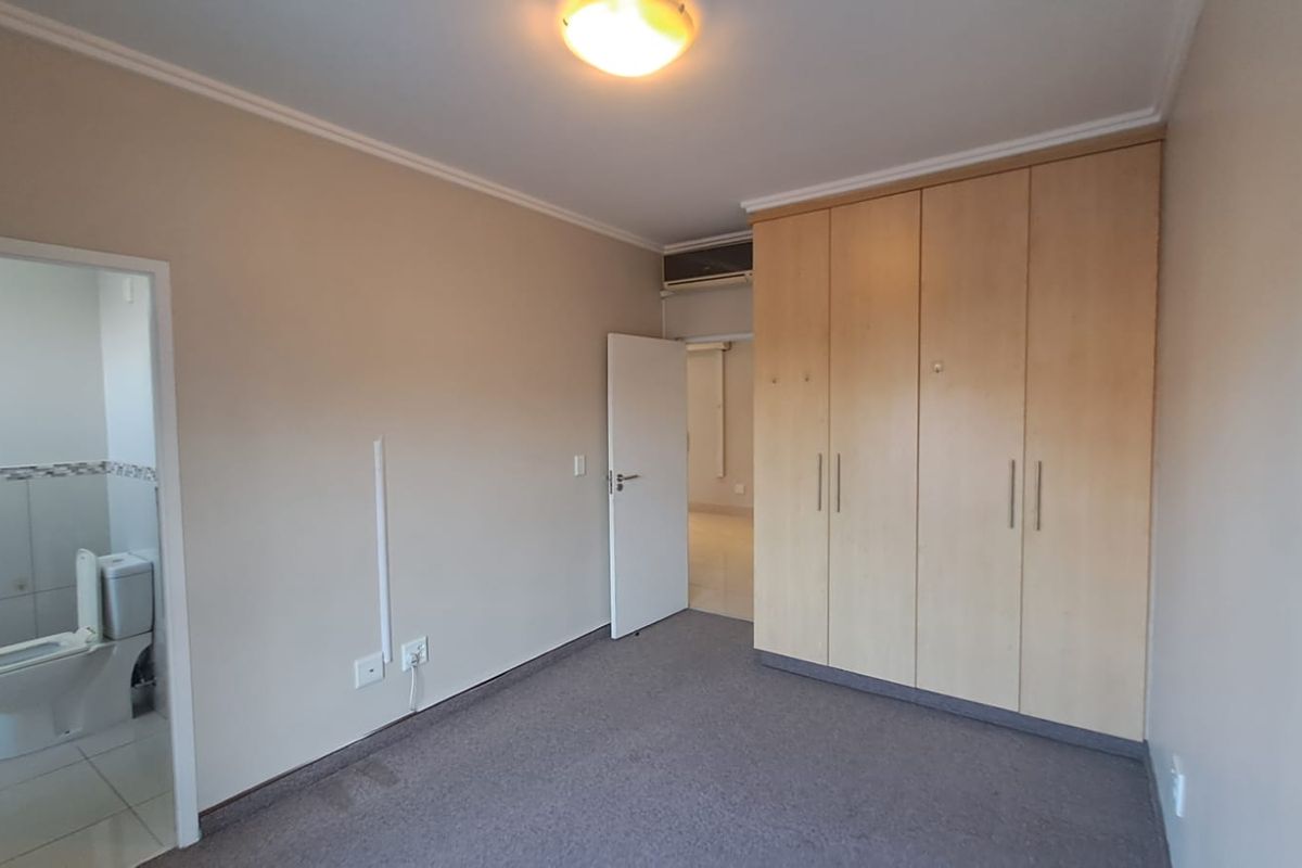 A spacious bedroom featuring neutral walls, carpeted flooring, and ample built-in cupboard storage, with an adjacent en-suite bathroom visible.